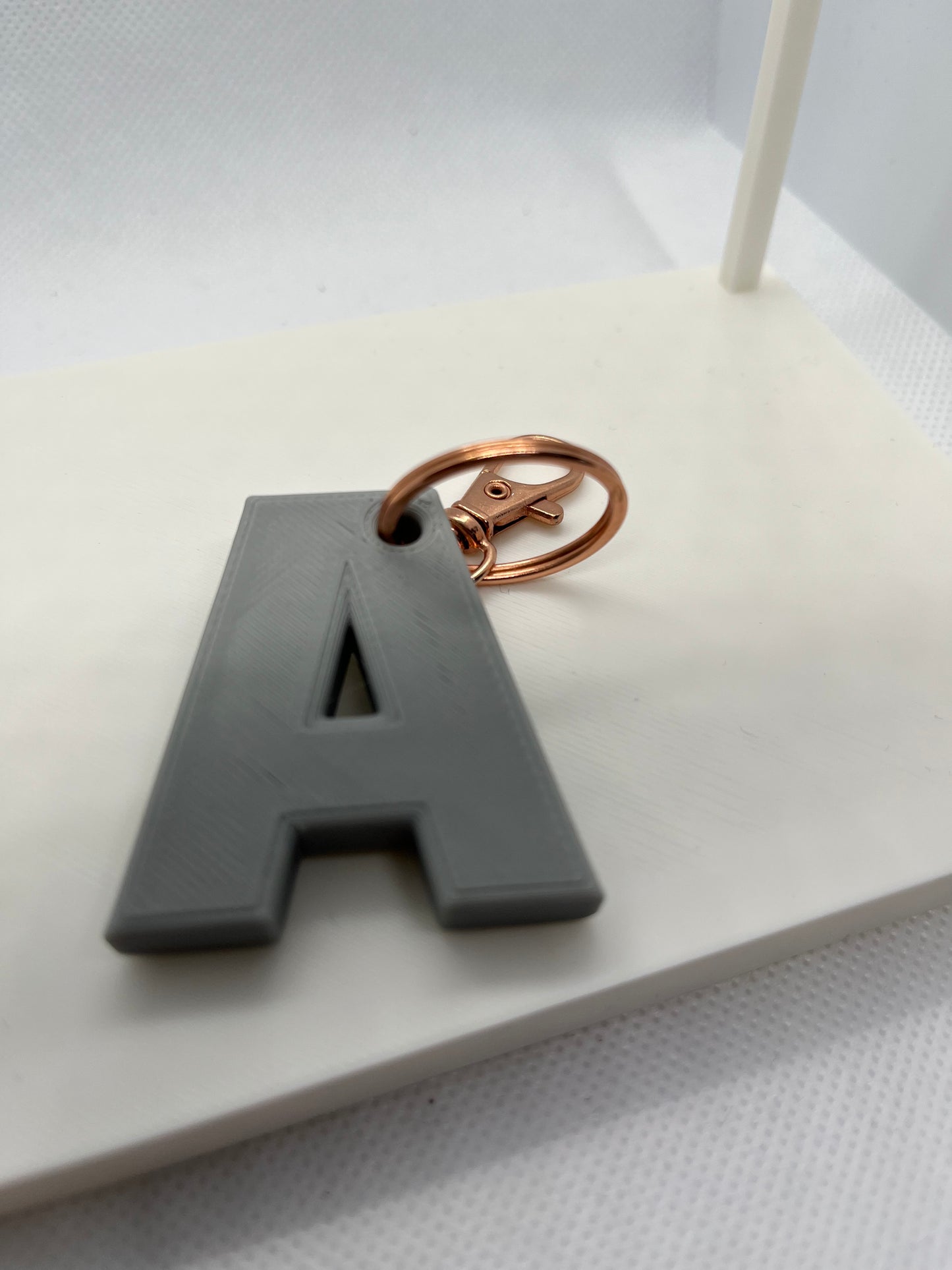 Gray letter 'A' keychain with a rose gold ring on a white background