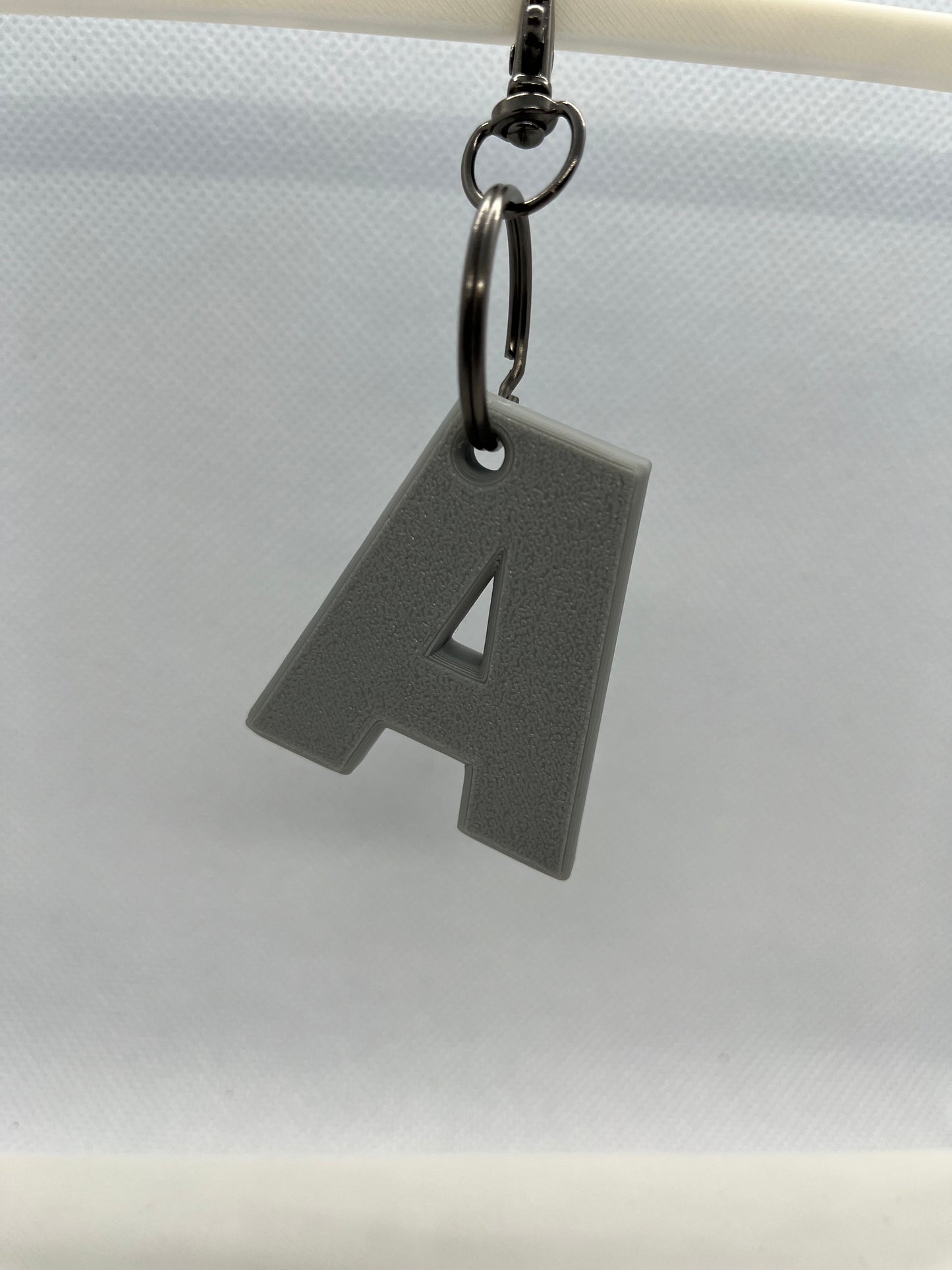 Gray letter 'A' keychain attached to a white curtain