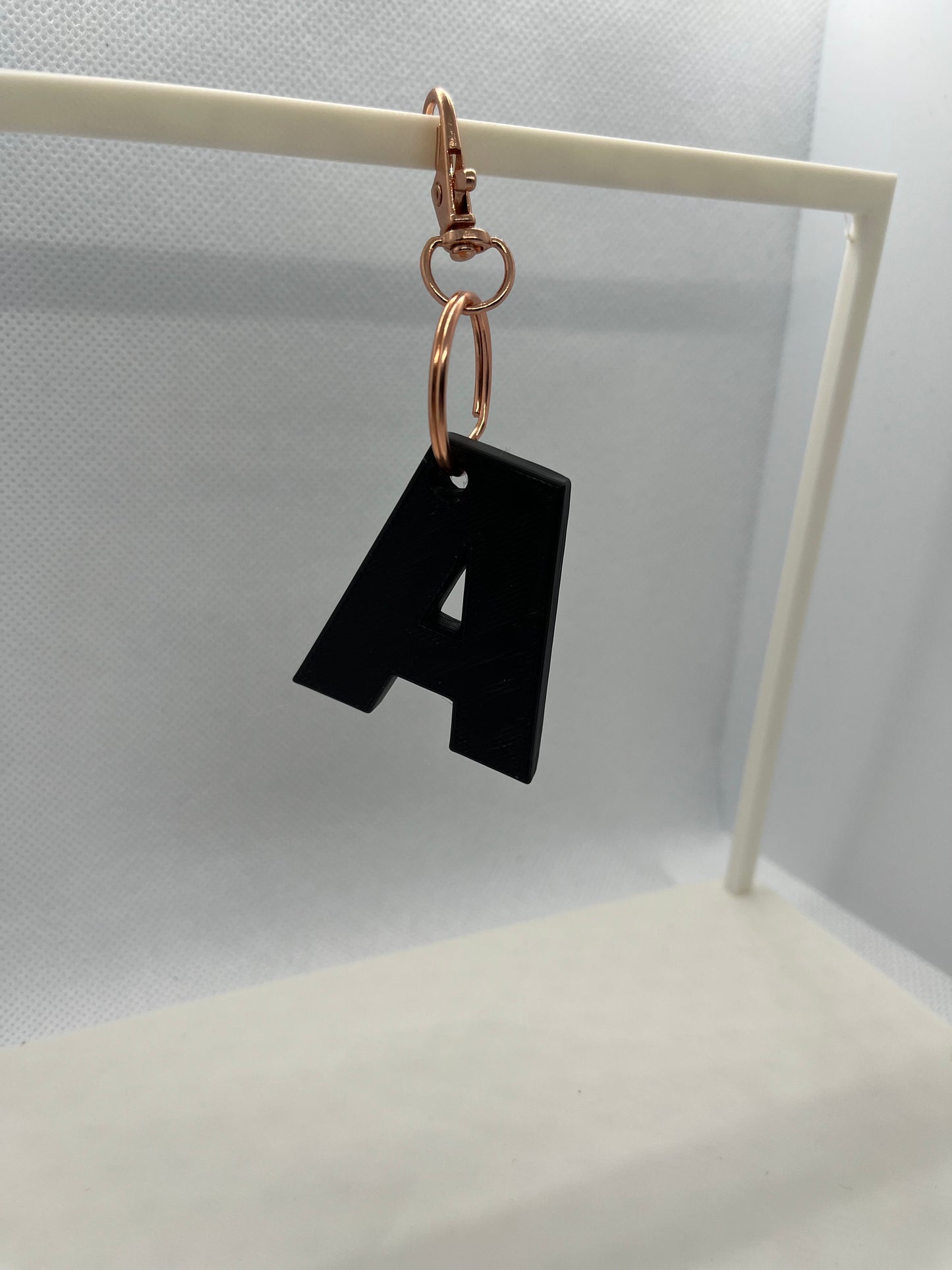 Black letter 'A' keychain on a white stand against a light gray background