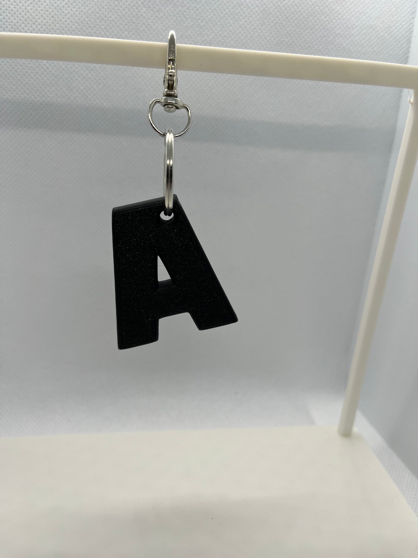 Black letter 'A' keychain on a white stand against a light gray background