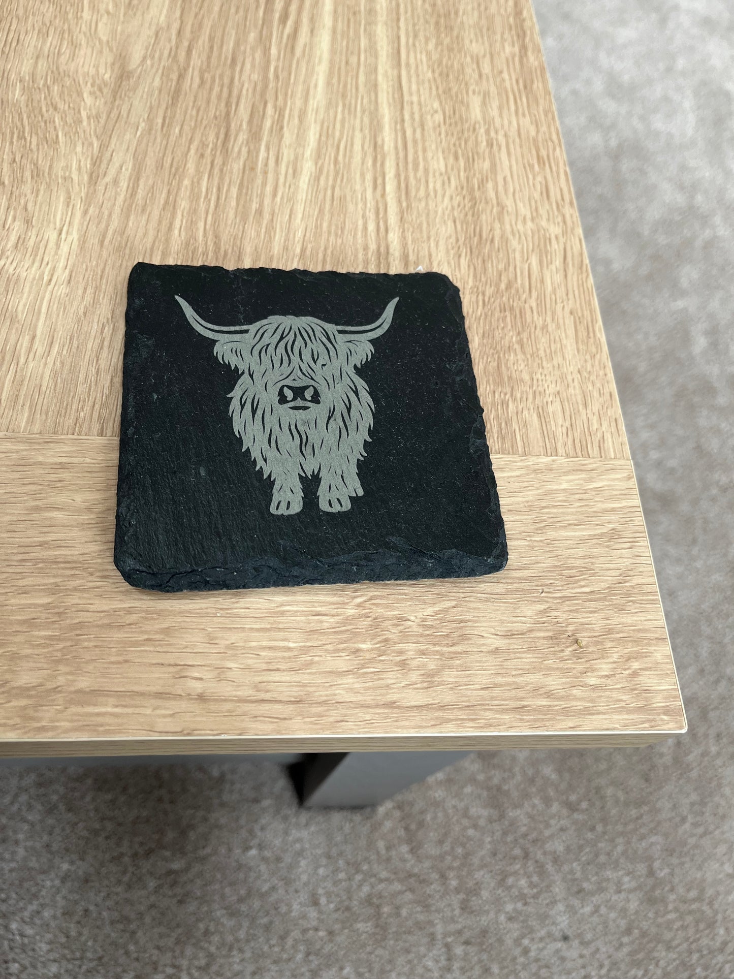 Black coaster with engraved design on a wooden surface