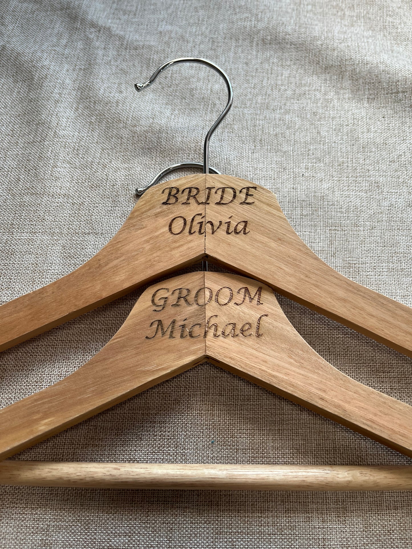 Two wooden hangers with engraved names on a textured fabric background