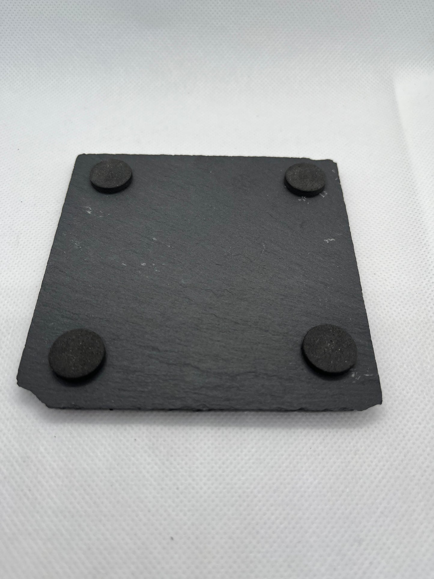 Black square slate coaster underside with 4 pads on a white background