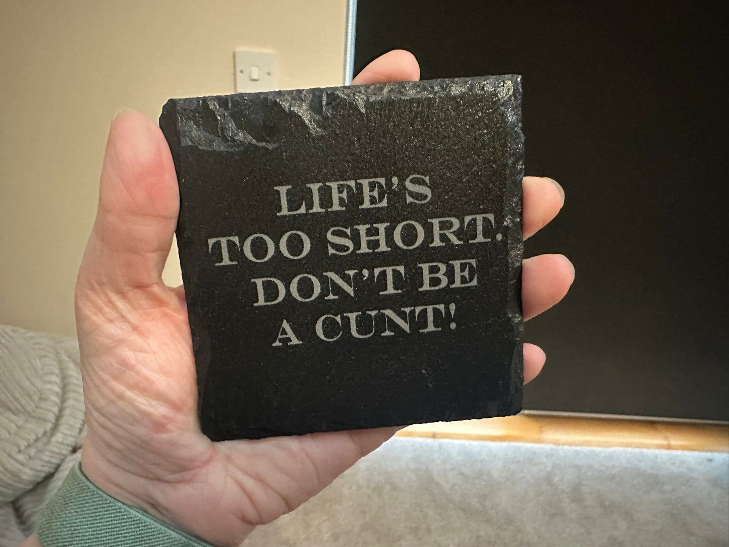 Black stone coaster with text held in a hand, against a neutral background
