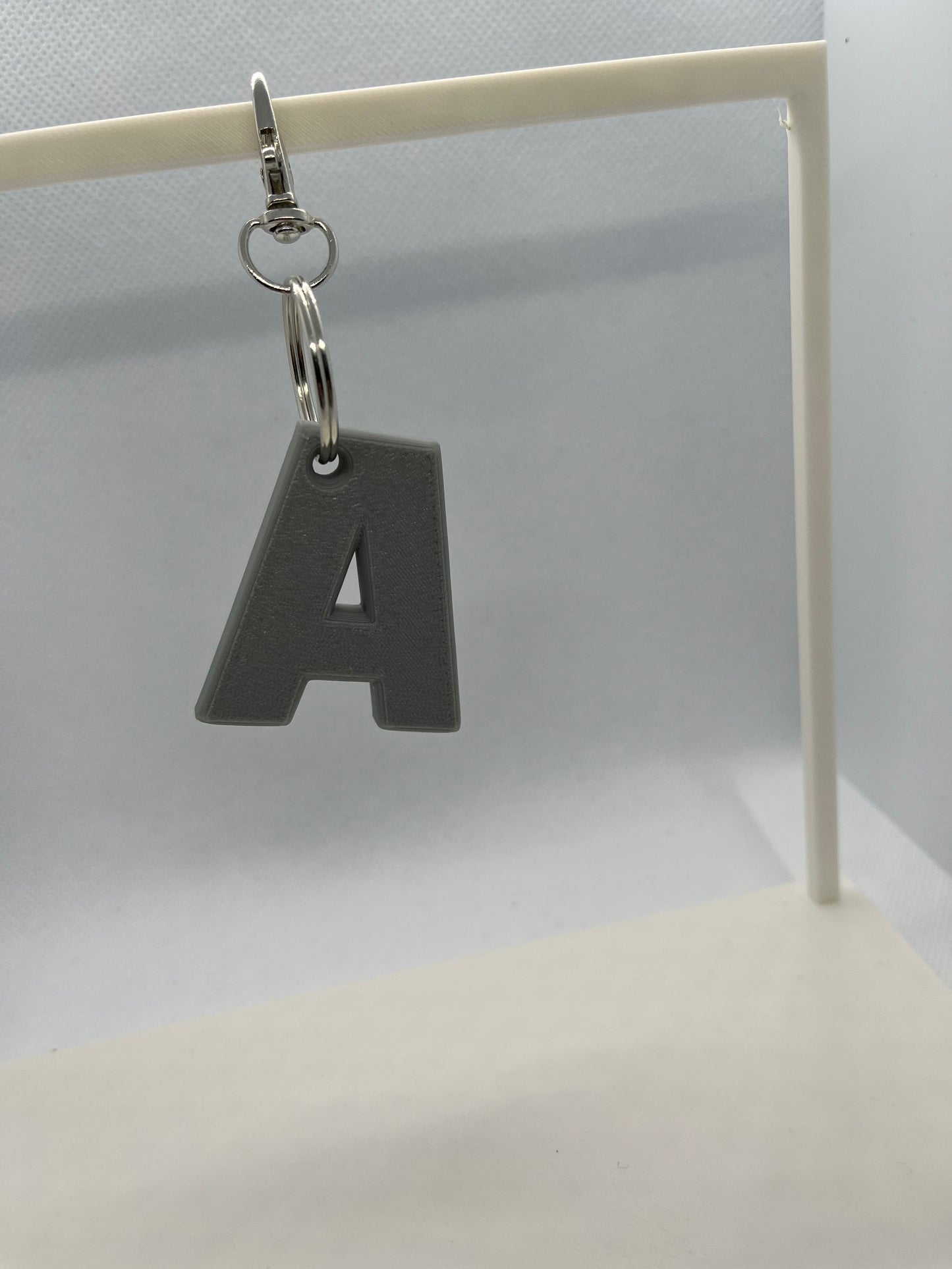 Grey letter 'A' keychain on a white stand against a white background