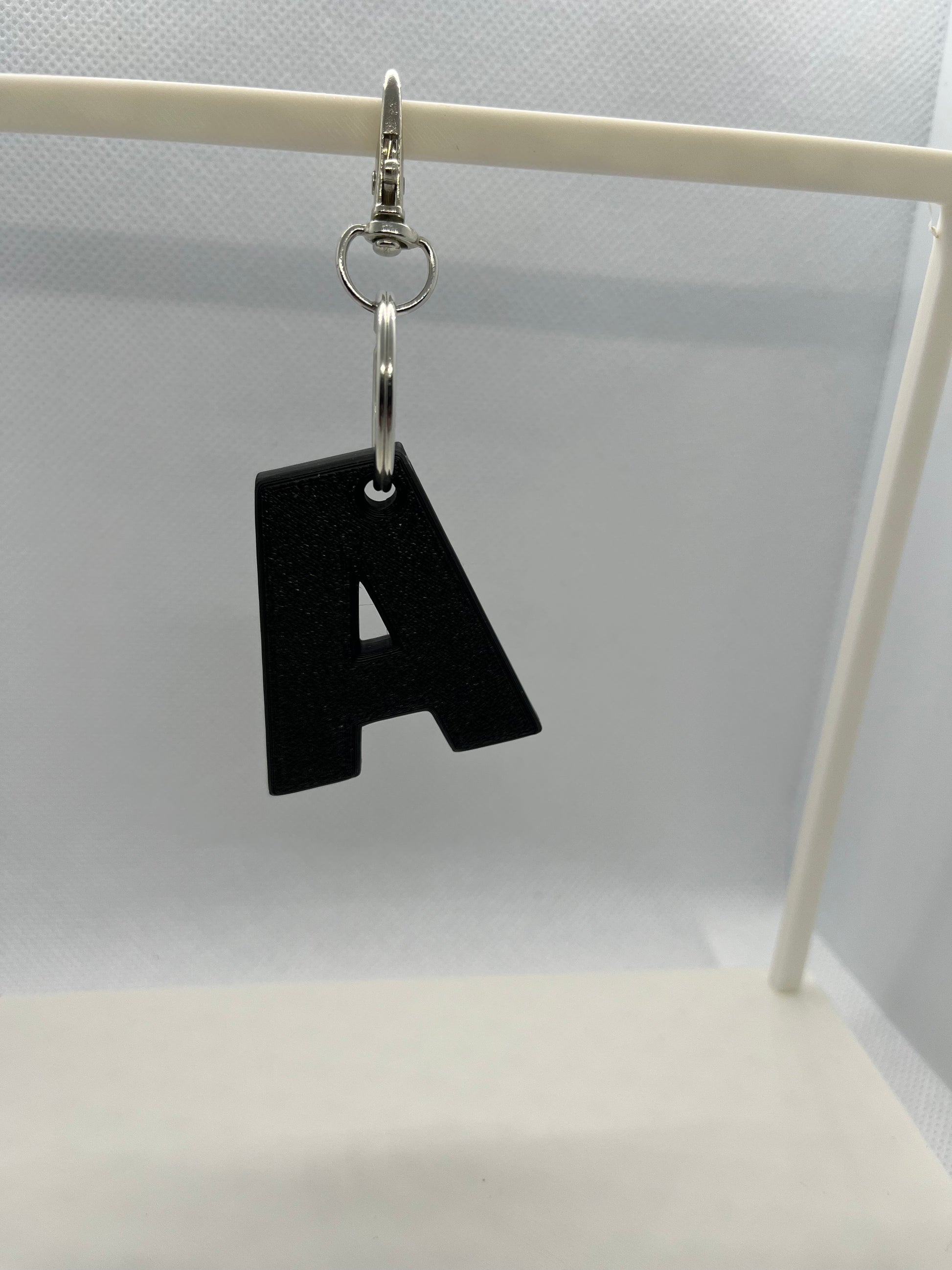 Black letter 'A' keychain on a white stand against a light gray background