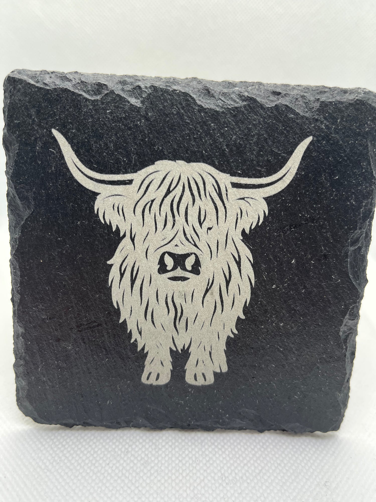 Slate coaster with engraved design of a fluffy creature on a white background