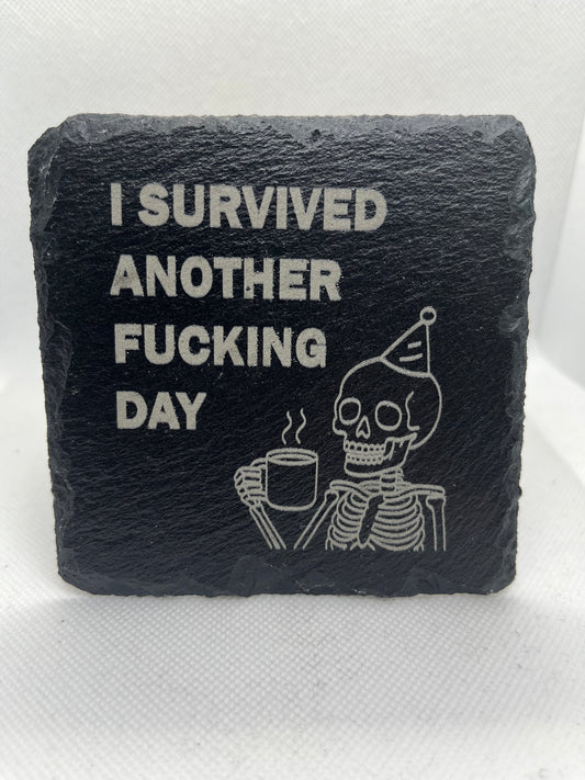 Black slate coaster with engraved text and skull design on a white background