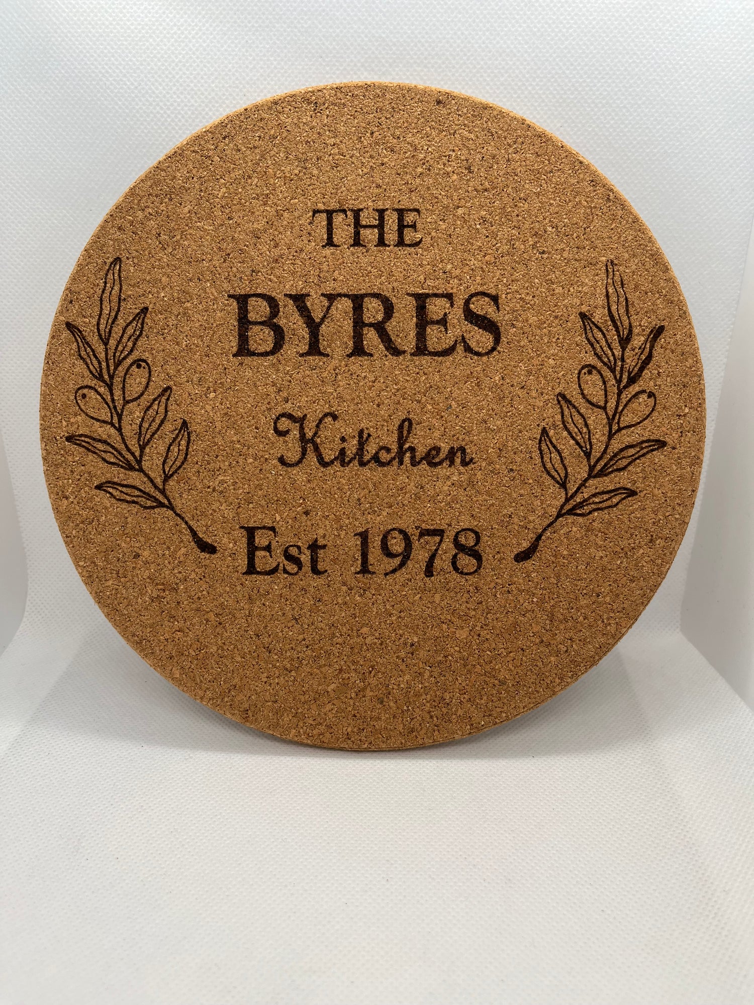 Round cork coaster with engraved text and leaf design on a white background
