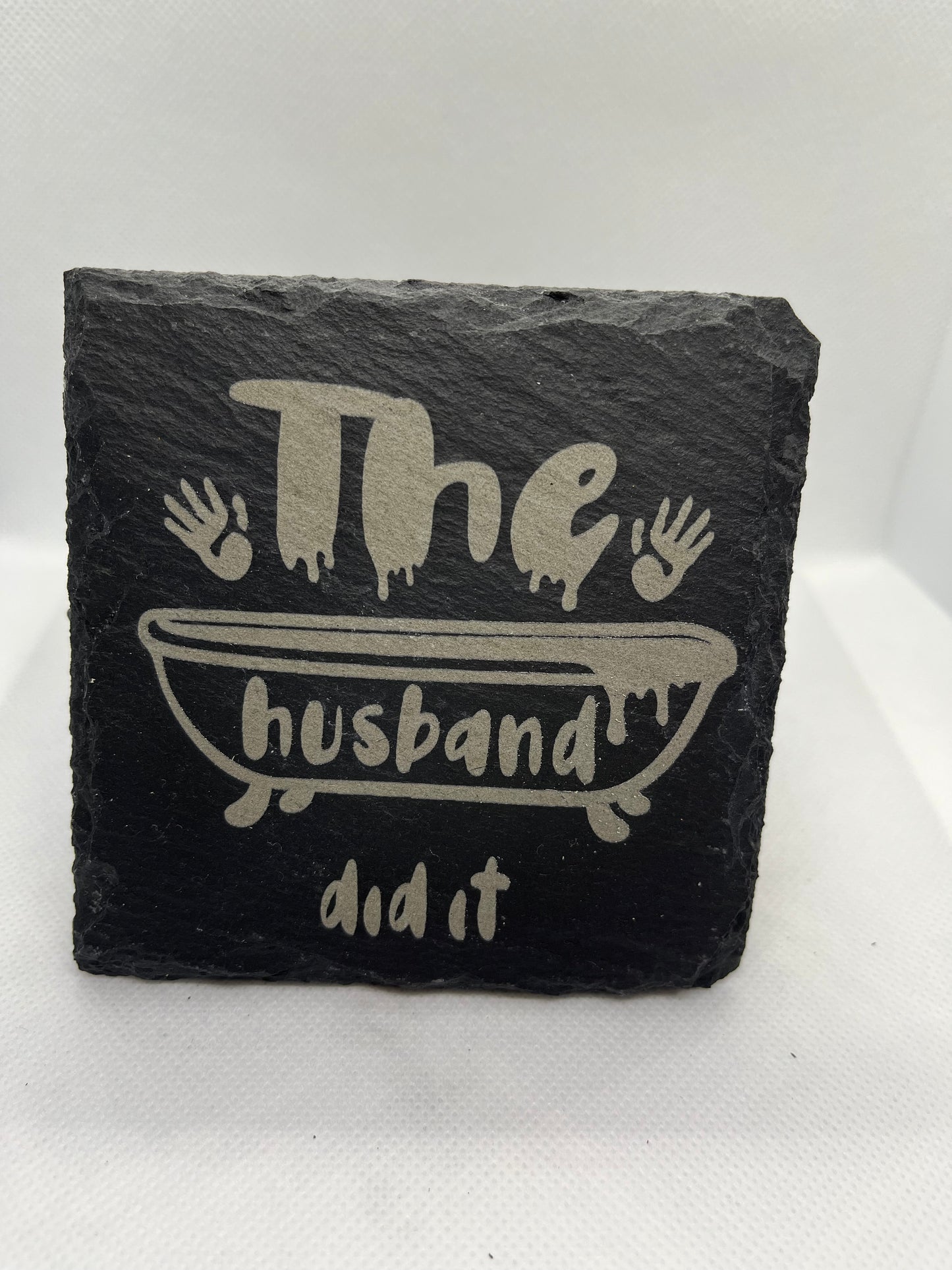 Black slate coaster with 'the husband did it' engraving on a white background